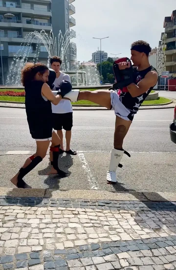 Atleta da Yoshinaga Fight Team a dar um pontapé alto aos pads do professor, ao ar livre junto a uma fonte em Oliveira de Azeméis